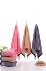 Detail of soft cotton towels in pink, grey, and brown with decorative white embroidery edge