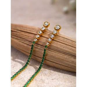 Macro detail of long tassel earrings with sparkling green and white crystals on wood