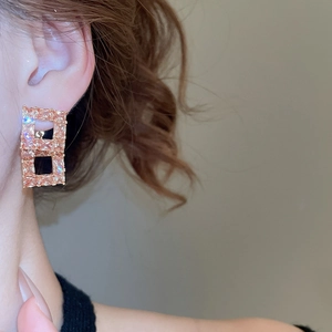 Close-up of geometric gold-plated earrings with pink crystal stones worn by a model