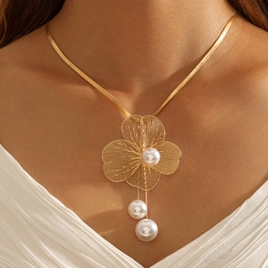 Détail d'un collier feuille de ginkgo doré avec perles élégantes et pompon sur chaîne serpent