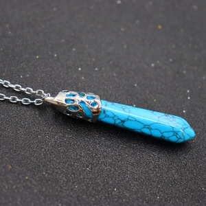 Macro detail of hexagonal turquoise crystal pendant with ornate hollow metal cap and chain