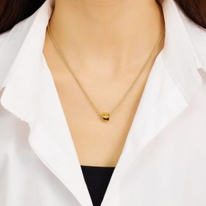 Close-up of a gold-plated necklace with a minimalist cube pendant on a model's neck