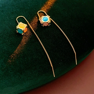 Detail view of gold-plated long chain earrings with colorful gemstone cube drops