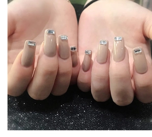 Close-up of nude trapezoid press-on nails with rectangular crystal accents on hand