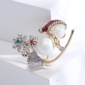 Close-up of pearl snowman brooch with red enamel hat and snowflake detail on white stand