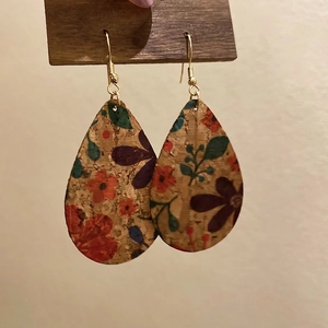 Floral print teardrop cork earrings with gold hooks on a wooden display stand