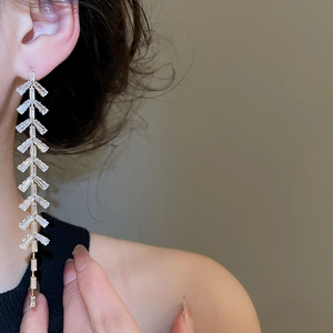 Gros plan de boucles d'oreilles pendantes dorées avec oxydes de zirconium en forme de feuilles