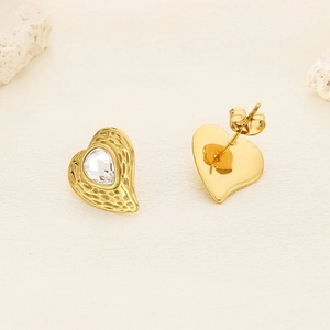 Orecchini a cuore dorati con texture martellata e cristallo su fondo in pietra