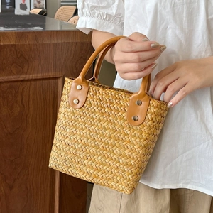 Close-up of woven straw handbag featuring brown leather handles and metal rivet details