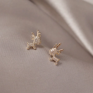 Macro shot of gold reindeer stud earrings with sparkling crystals on silk fabric