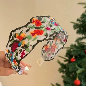 Detailed close-up of white mesh headband with colorful floral embroidery on a wide band