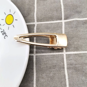 Detail of a minimalist gold alloy duckbill hair clip with a brushed metal texture