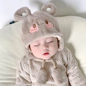 Dettaglio del cappello in peluche kaki per neonati con paraorecchie e lacci con pompon