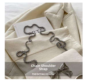 Detail of silver butterfly buckle and metallic ball chain strap on cream handbag