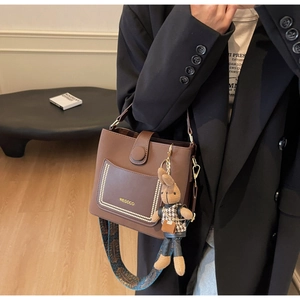 Detail of dark brown bucket bag with bohemian wide strap and plush bunny charm