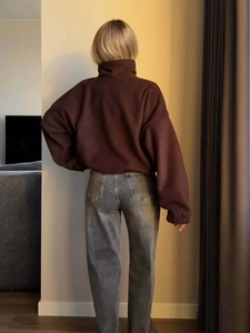 Back view of a woman in a brown fleece yoga jacket and grey jeans in a cozy room