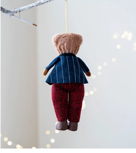 Detailed plush bear charm in blue striped jacket hanging on a branch with bokeh lights