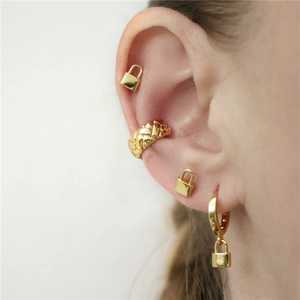 Detailed view of gold padlock stud earrings and woven cuff earring set worn on ear