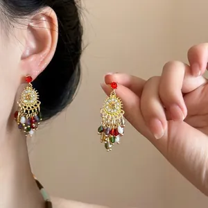 Detail of bohemian gold earrings with red stones and colorful beaded feather tassels
