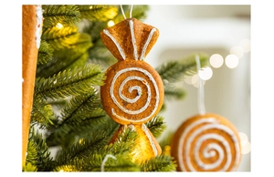 Close-up of a gingerbread candy ornament with white spirals hanging on a glowing tree