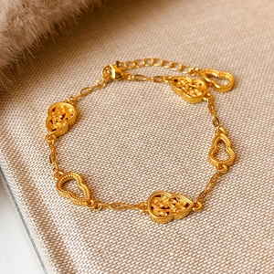 Vergoldetes Armband mit Herzanhängern und floralem Filigran-Muster auf feiner Textur