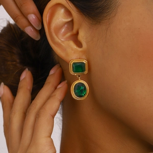 Close-up of elegant gold earrings with green emerald-cut stones worn by a woman