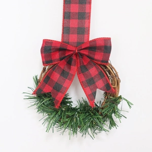 Christmas wreath with red black buffalo plaid bow and green pine needles on grapevine
