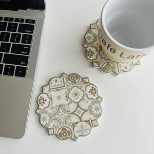 Top view of two bohemian octagonal ceramic coasters with gold mandala patterns on a desk