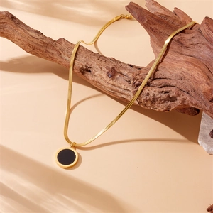 Vintage gold snake chain necklace with black Roman round pendant on driftwood