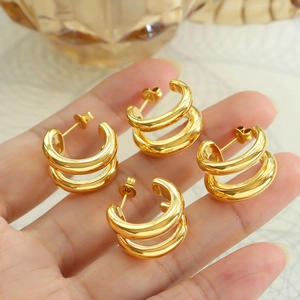 Handheld display of gold double C-shaped earrings with minimalist metallic texture
