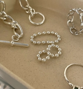 Detailed close-up of polished silver beaded ring and chain bracelet on a beige tray