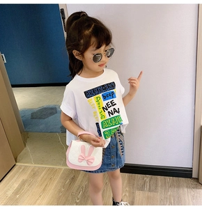 Detail view of little girl wearing white graphic T-shirt and denim skirt with cute handbag
