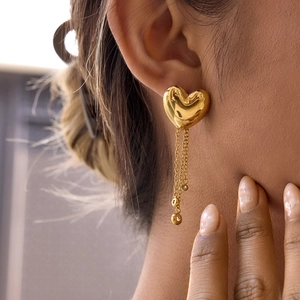 Close-up of golden heart earrings with long chain tassels worn by a female model