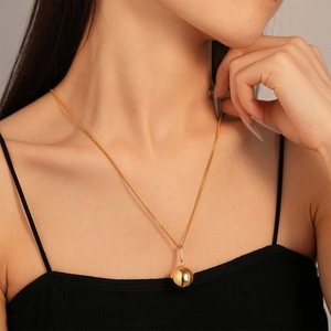 Gros plan d'un collier avec pendentif boule en or 18K poli porté avec un haut noir