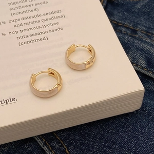 Élégantes créoles dorées avec insert blanc posées sur un livre pour un style minimaliste