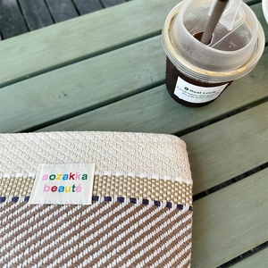 Detail of colorful striped woven makeup bag with fabric logo tag on a green wooden table