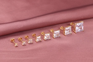 Set of 8 pairs of golden square zircon stud earrings in various sizes on pink silk