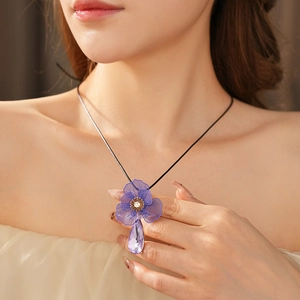 Detail view of flower-shaped pendant with teardrop purple crystal and black cord