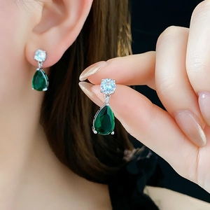 Detailed close-up of teardrop emerald zircon earrings with silver metal base on model