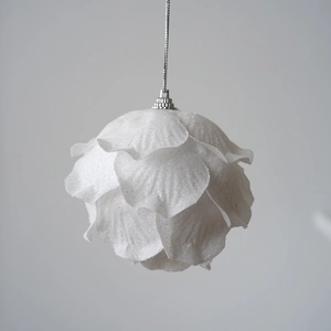 Close-up of a white petal-shaped Christmas ball with glitter and hanging silver loop