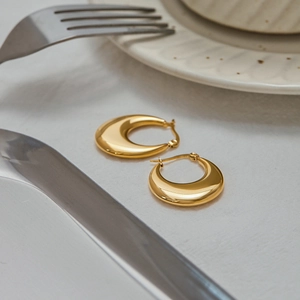 Close-up of gold titanium steel hoop earrings on a white napkin with a bright metallic finish