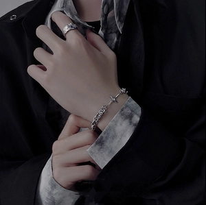 Detail of silver cross bracelet and blue gemstone ring on model wearing black fashion streetwear