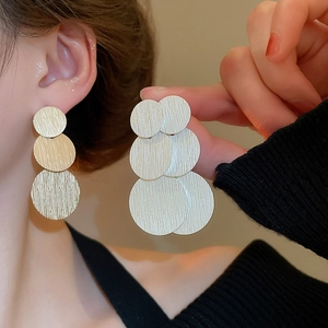 Golden geometric triple round brushed metal drop earrings worn by fashion model