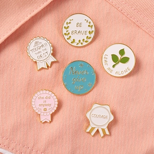 Set of 6 enamel pins with inspirational quotes like Be Brave on pink denim fabric