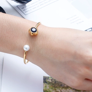 Close-up of golden open bangle with white pearl and navy blue flower gemstone on wrist