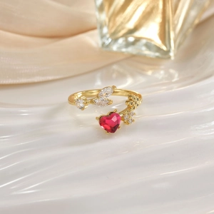 Close-up of golden adjustable ring with a red heart-shaped gemstone and floral details