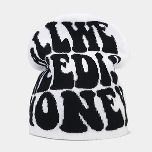 Close-up of white knitted beanie featuring black jacquard letters and knit texture