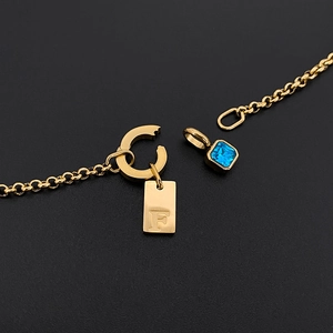 Vista detallada de un collar de acero inoxidable dorado con etiqueta F y cristal azul.
