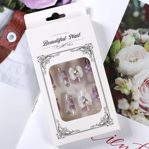 Detail of purple gradient press-on nails with white bow and rhinestones in gift box
