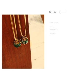 Close-up of emerald green zircon pendants on gold titanium steel chains over wood